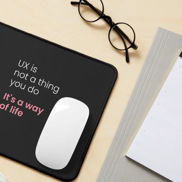 A pink mouse pad with the phrase "UX is not a thing you do, it&rsquo;s a way of life" in white and pink letters.