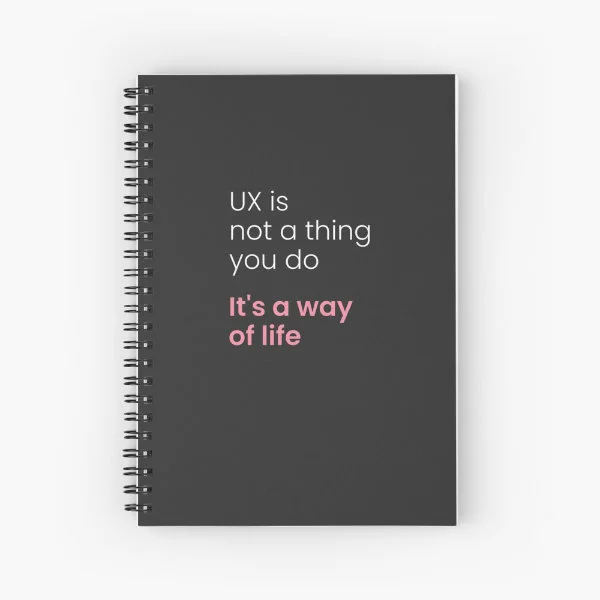 A spiral notebook with the phrase "UX is not a thing you do, it&rsquo;s a way of life" in white and pink letters.